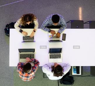 Aerial view of four students working together on laptops at a table in the Gatton Student Center.