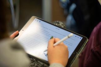 Up-close photo of student writing on an iPad with a stylus pen.