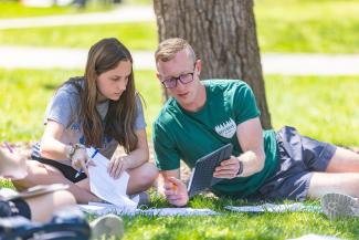 Photo of students looking at an iPad while sitting outside during class time.